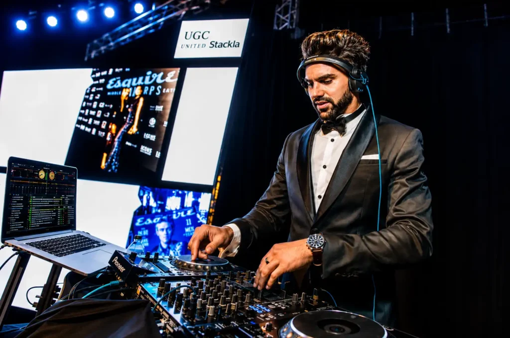 Professional DJ performing at a corporate event while mixing music on a Pioneer DJ setup in front of a large LED screen.